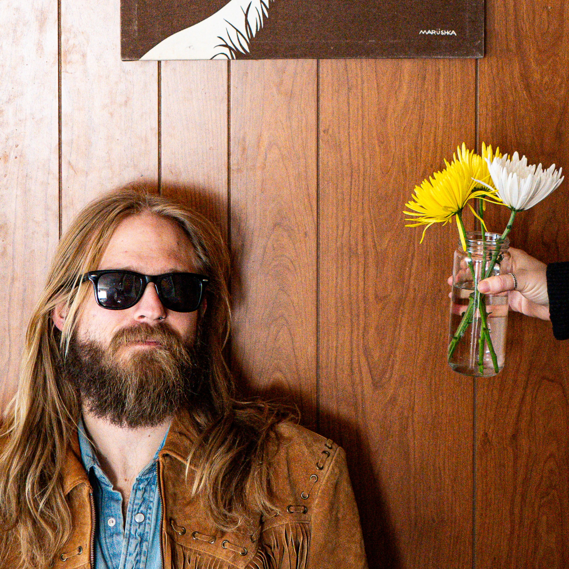 Portrait against wood paneling with a jar of daisies