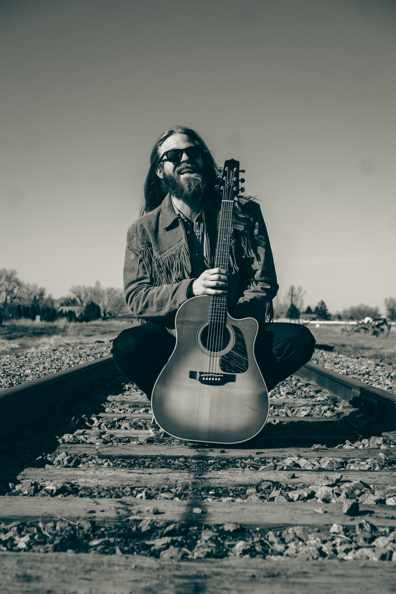 Duotone portrait seated on the tracks with guitar